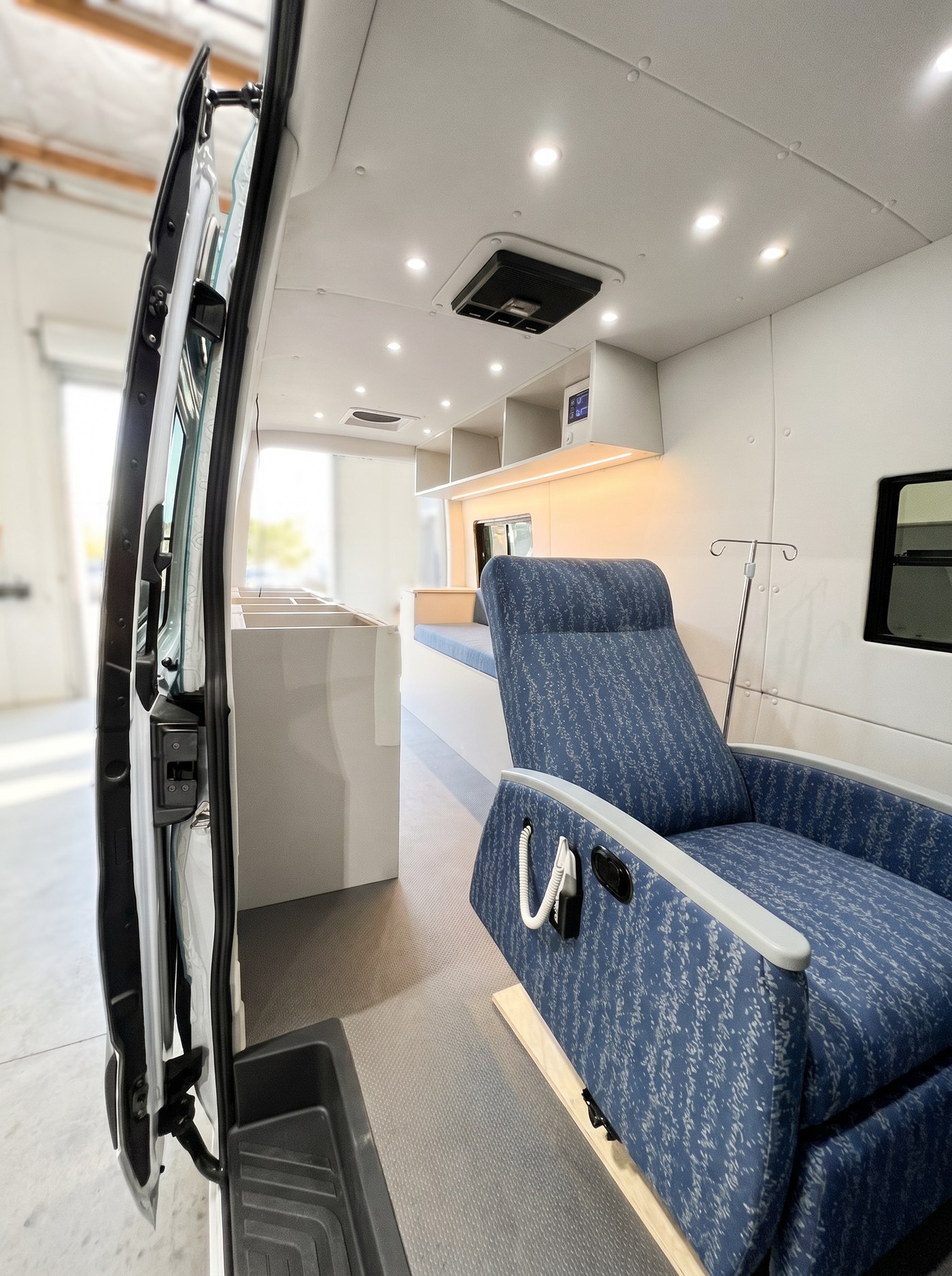Interior of a QSC mobile infusion van &mdash; patient recliner with IV pole, overhead clinical lighting, monitor, prep counters and storage